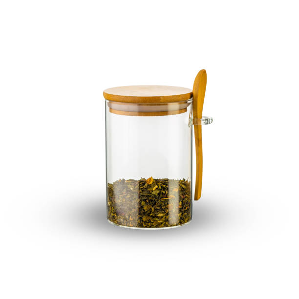 Glass jar and wooden spoon with tea leaves isolated on white