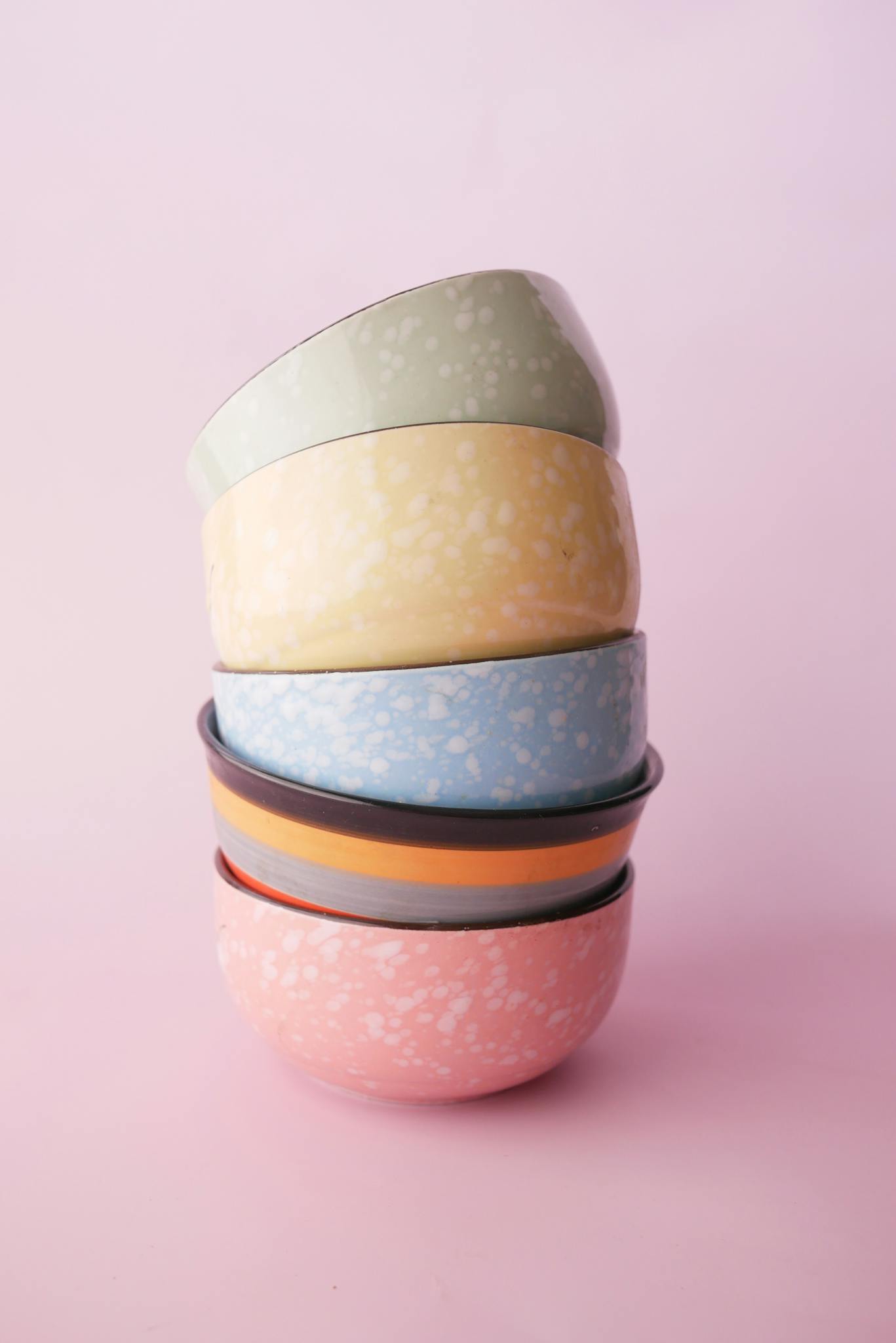 Colorful ceramic bowls stacked on soft pink background, perfect for elegant tableware displays.