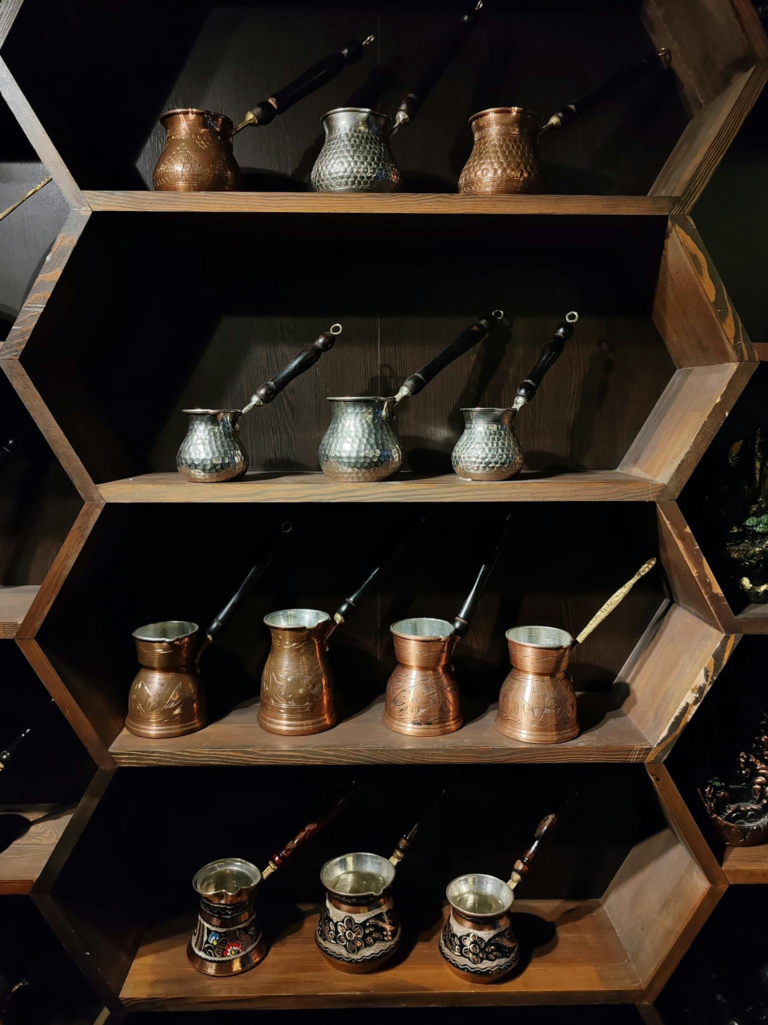 Display of traditional copper coffee pots on elegant wooden hexagonal shelves.