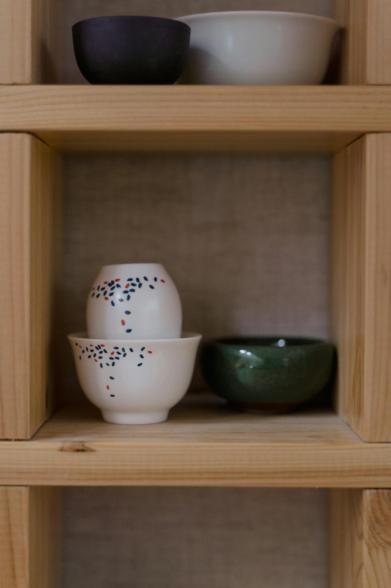 Minimalist display of Asian ceramic cups and bowls on a wooden shelf.